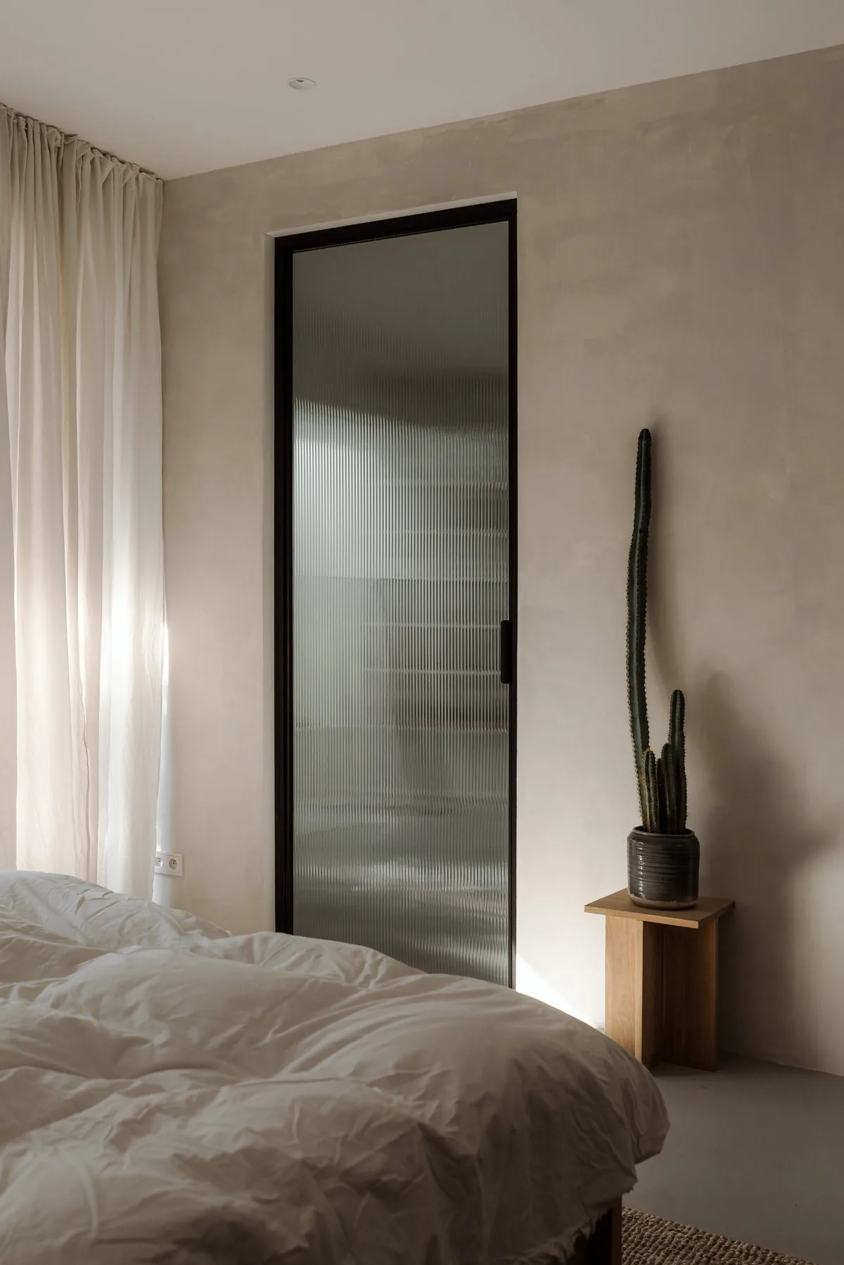 Dormitorio minimalista con puerta de vidrio canalado y luz cálida